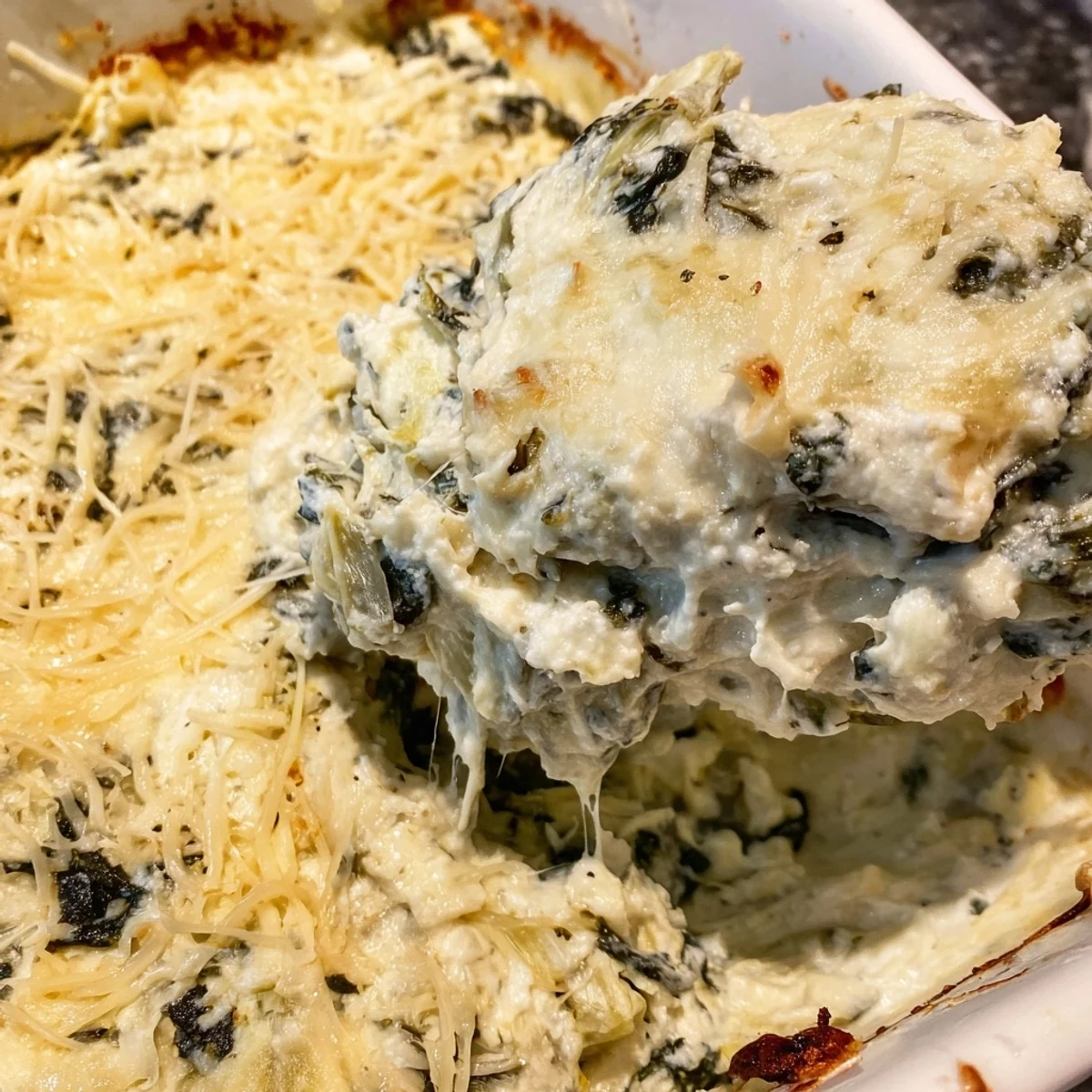 A close-up of a warm, golden Creamy Spinach and Artichoke Dip, perfect for dipping crackers or veggies.