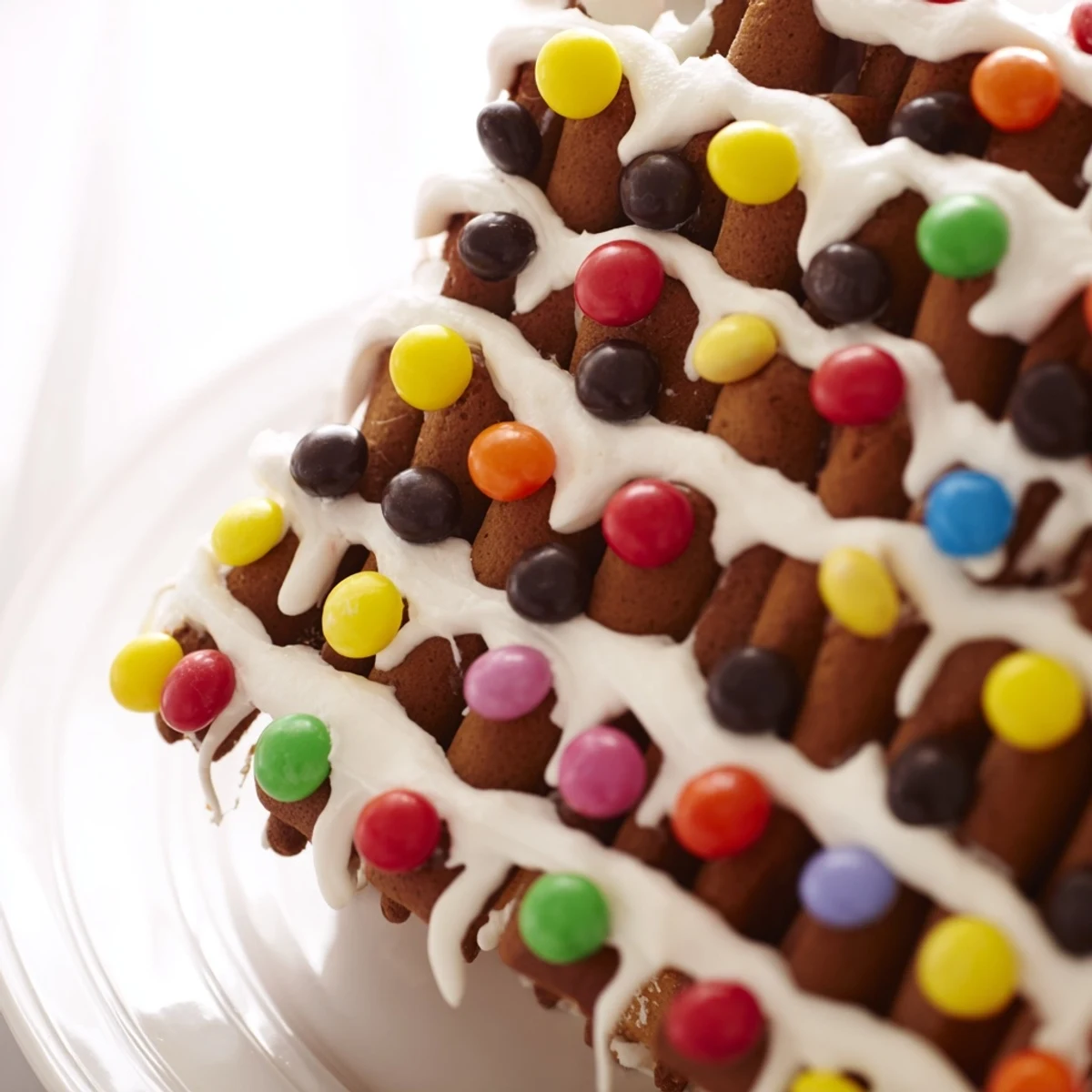 A fully assembled Gingerbread House Decor with Candy shows royal icing roof tiles, candy cane chimney, and colorful M&M window frames, ready for family fun.
