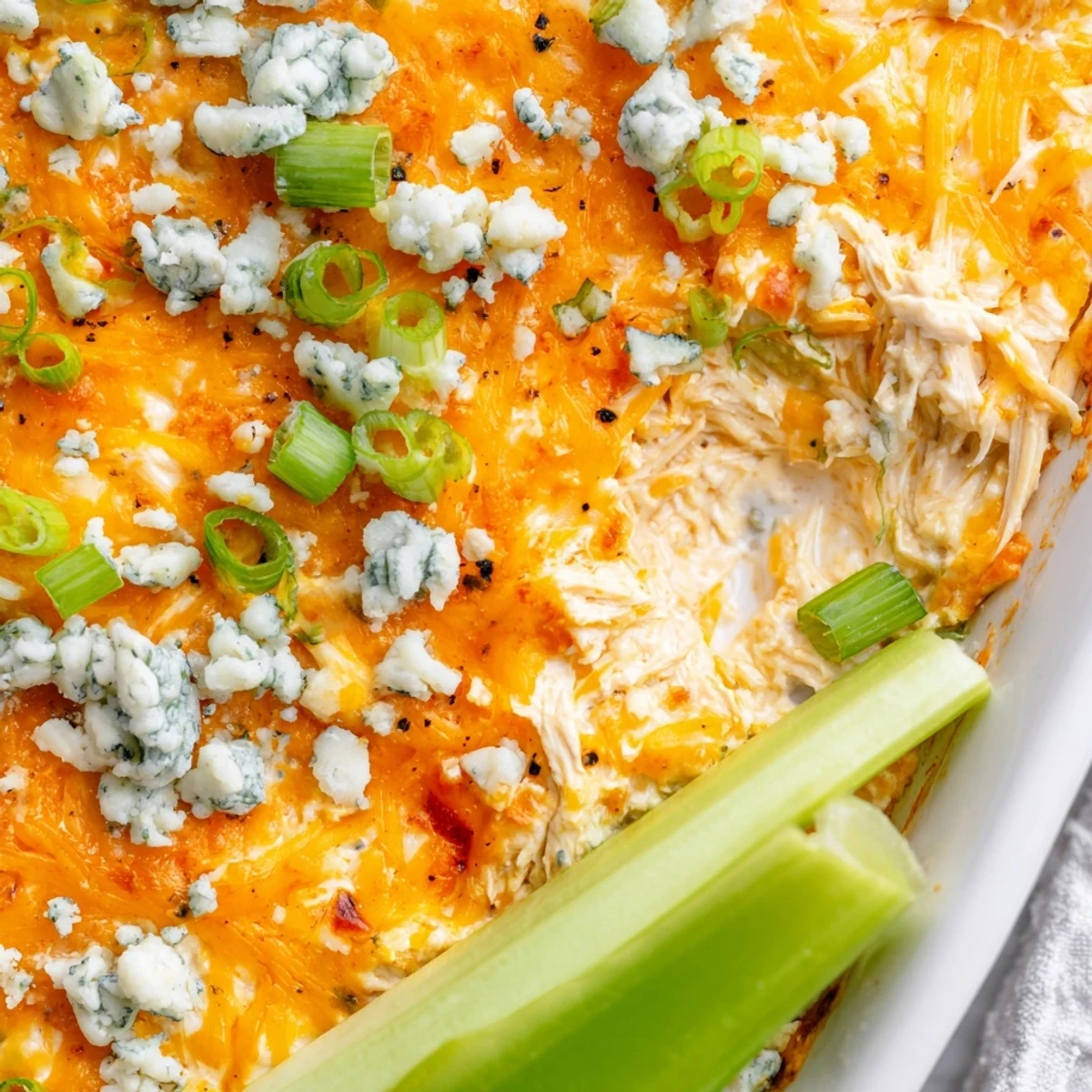 Golden, bubbly Spicy Buffalo Chicken Dip in a baking dish, with crisp celery sticks arranged around the edge for dipping.