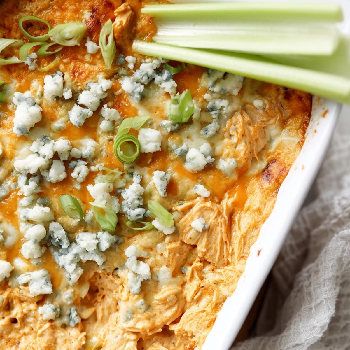 Golden-brown Spicy Buffalo Chicken Dip in a casserole dish, garnished with chives and ready for celery dipping at a party.