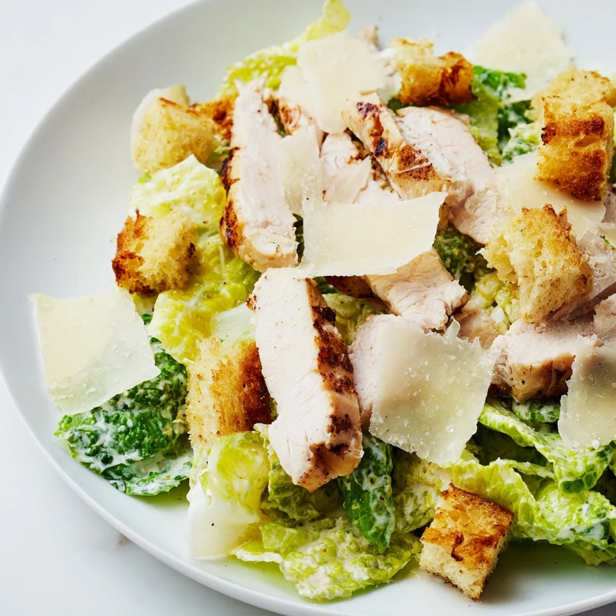 Tongs lift a hearty serving of Chicken Caesar Salad with Homemade Croutons, drizzled with creamy dressing.