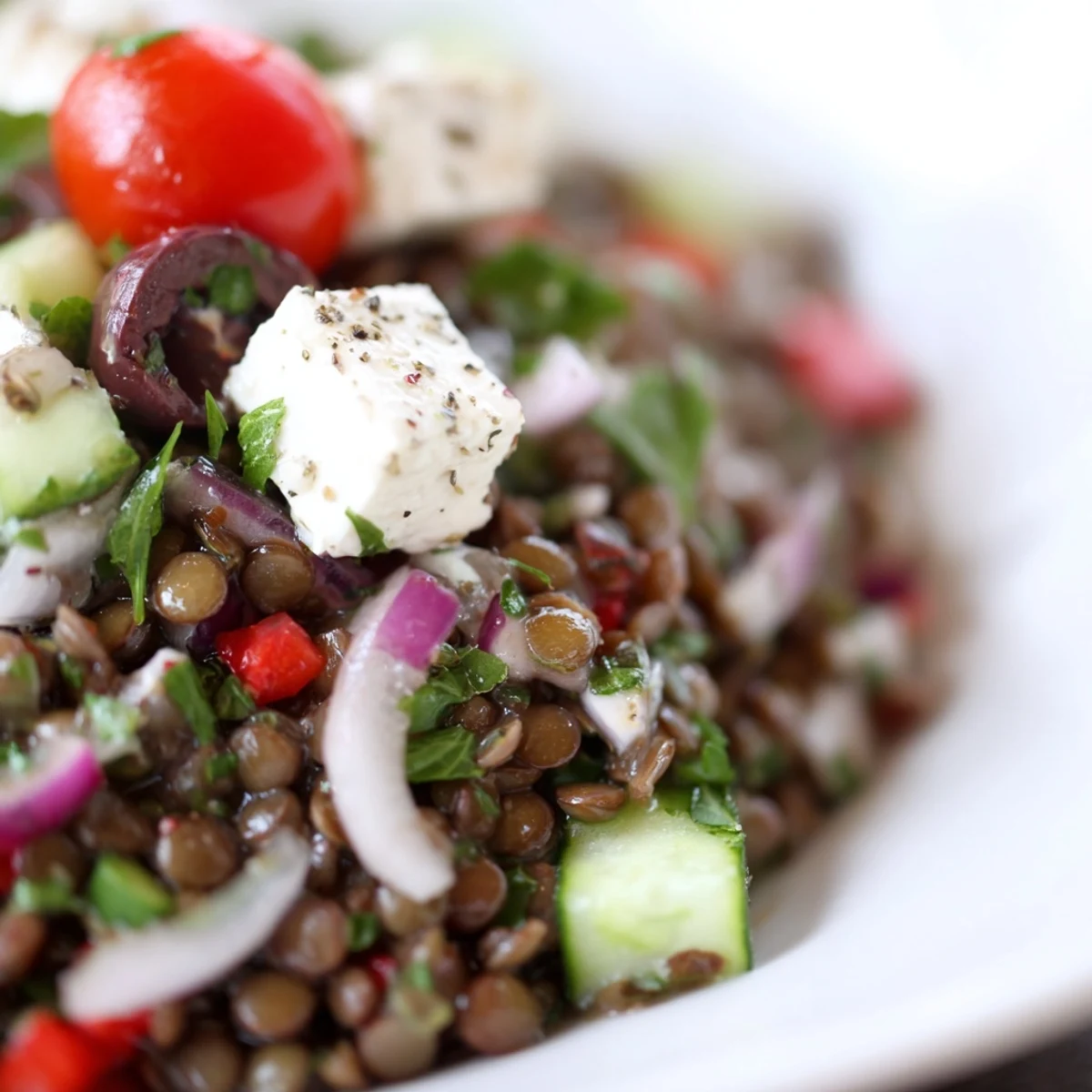 Colorful bowl of Mediterranean Lentil Salad topped with crumbled feta, Kalamata olives, and fresh herbs.