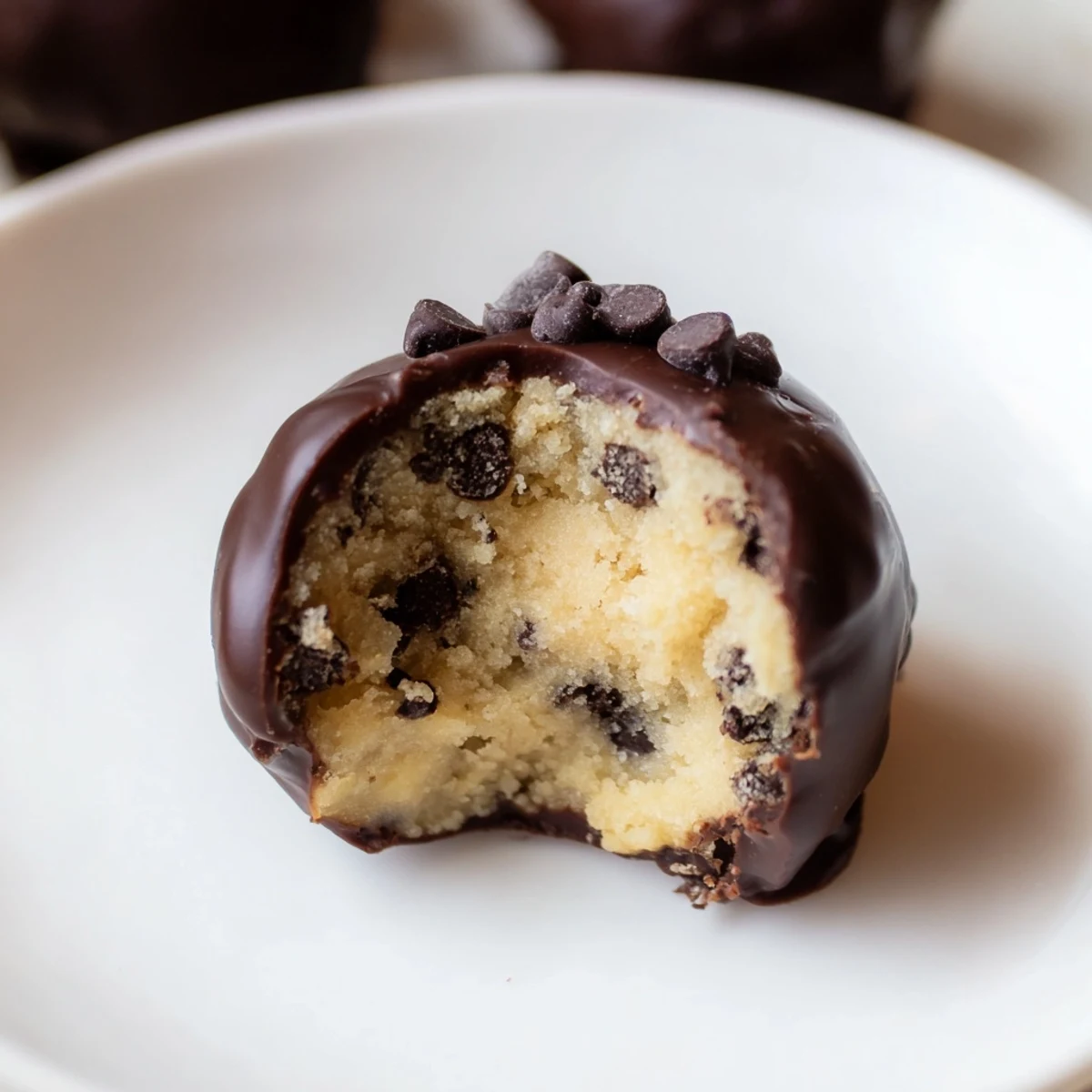 A close-up of golden-brown chocolate chip cookie dough truffles nestled in a mini baking cup, drizzled with melted chocolate.