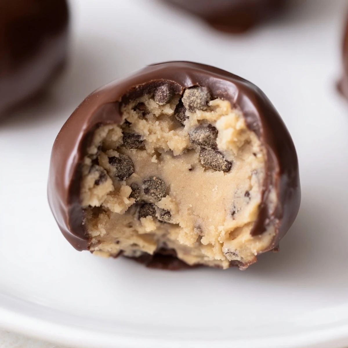 A single bite-sized chocolate chip cookie dough truffle sits on a wooden board, showcasing the creamy cookie dough center.