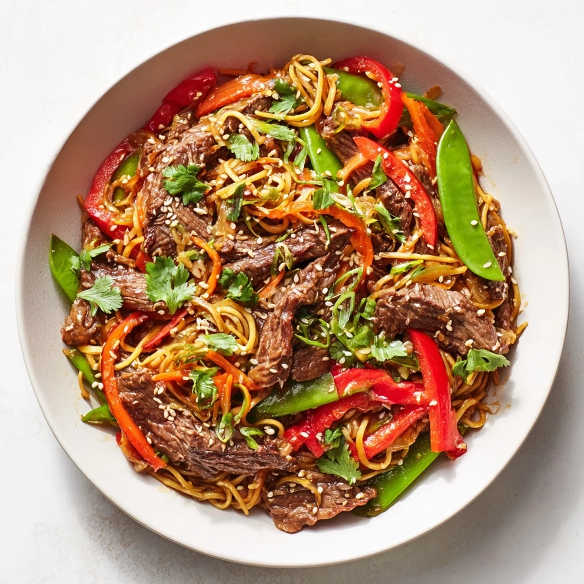 Spicy beef stir fry with noodles tossed with colorful bell peppers, carrots, and snap peas served on white ceramic bowls.