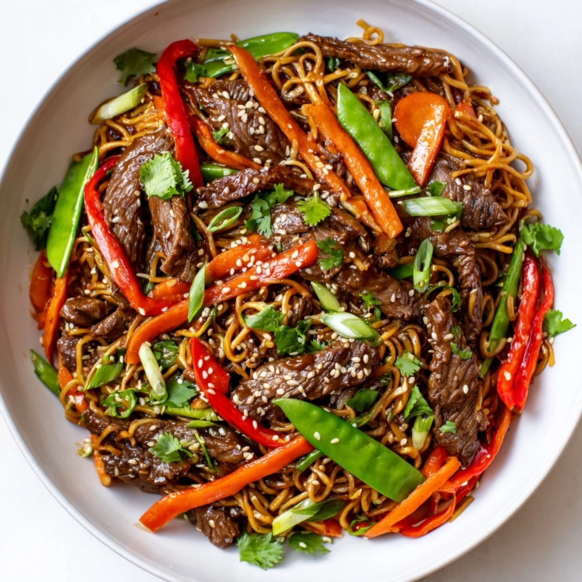 Quick weeknight spicy beef stir fry with noodles garnished with sesame seeds and cilantro, ready to serve with lime wedges.