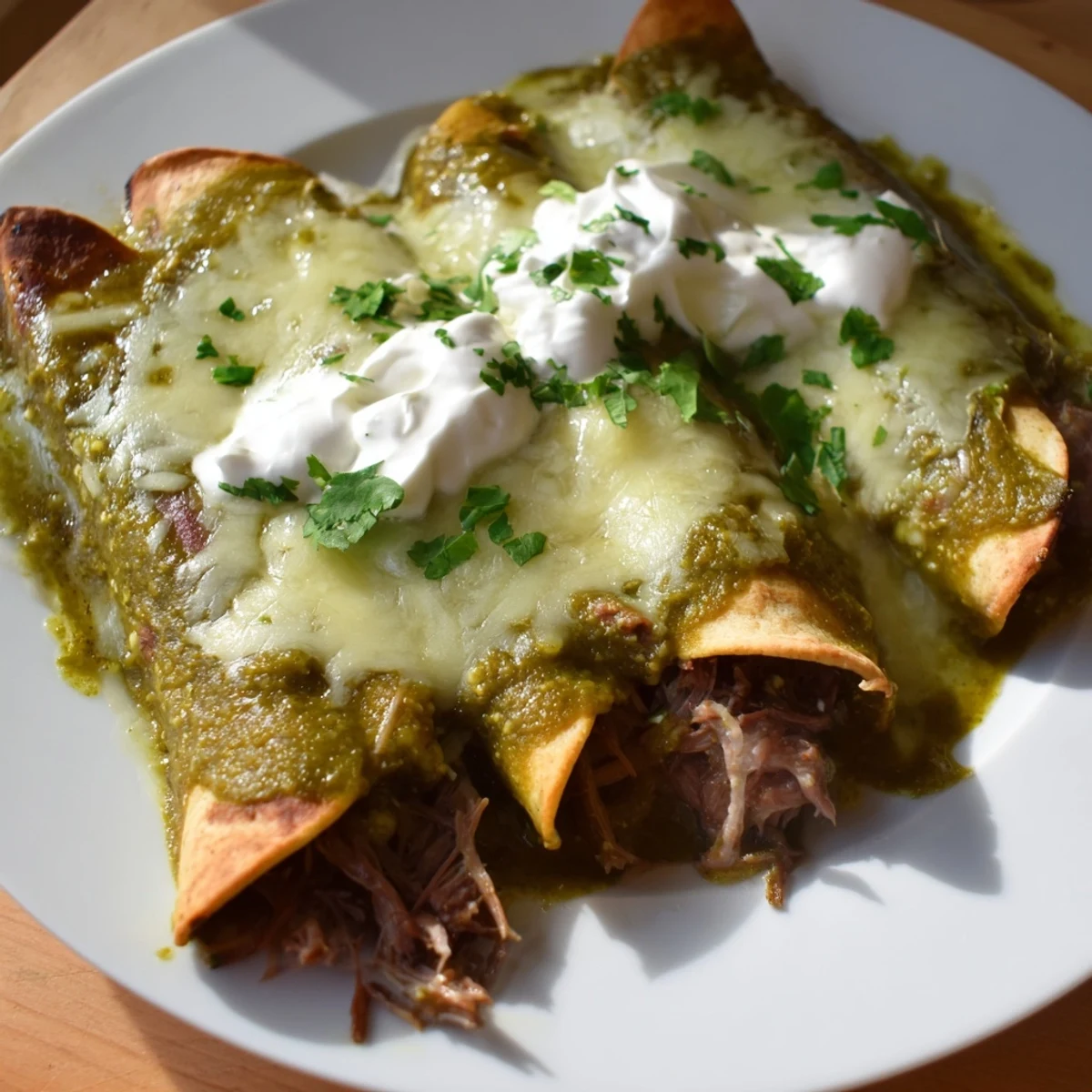 Golden, melted cheese blankets these soft corn tortillas filled with tender shredded beef, all smothered in a vibrant green tomatillo sauce.
