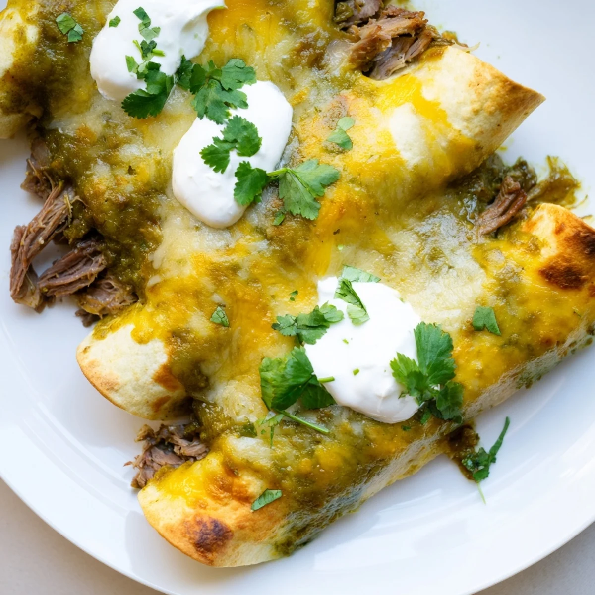 A close-up of baked Beef Enchiladas with Green Sauce, garnished with fresh cilantro and a dollop of sour cream.