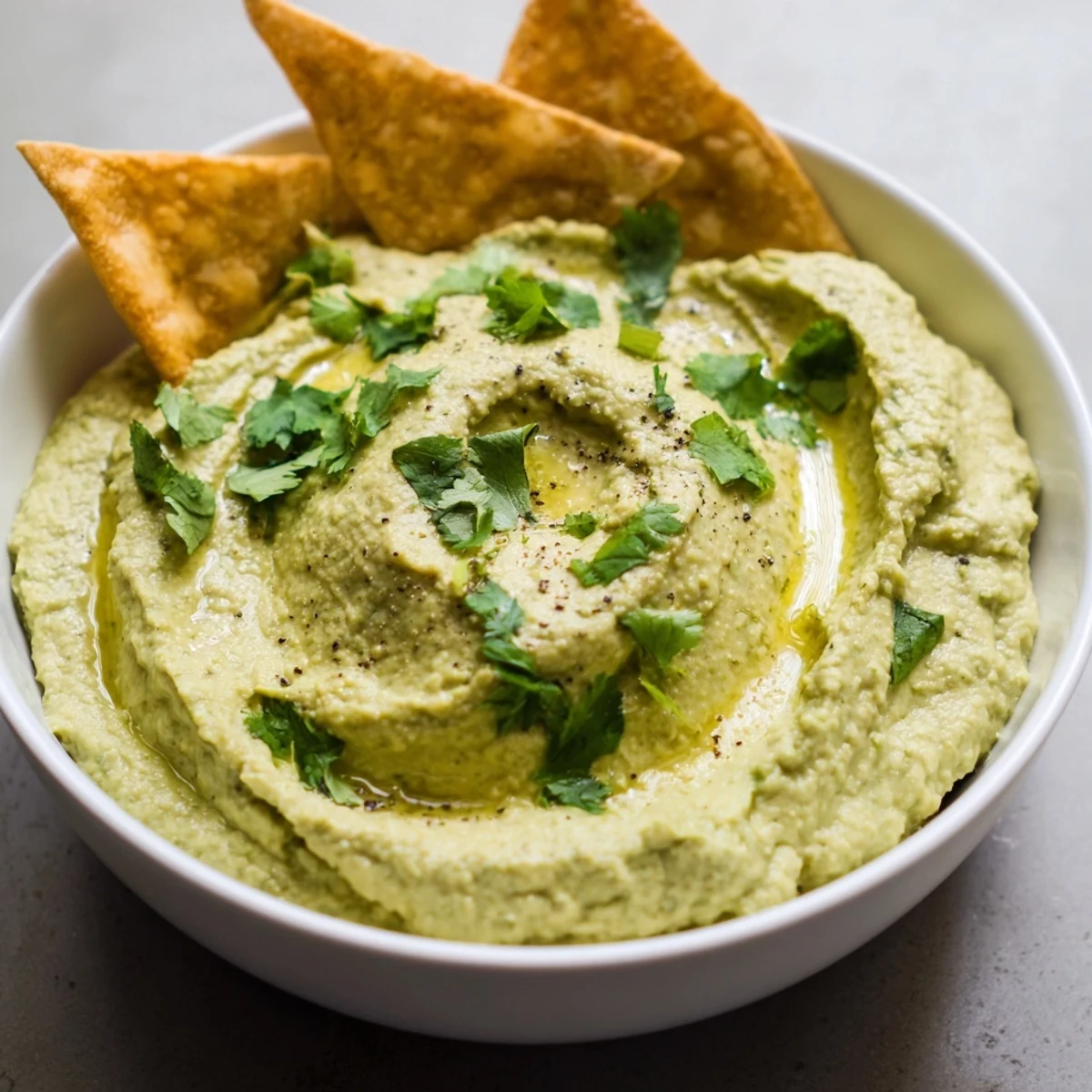 Bright avocado hummus blend with fresh herbs in a rustic bowl, alongside toasted pita triangles perfect for snacking.