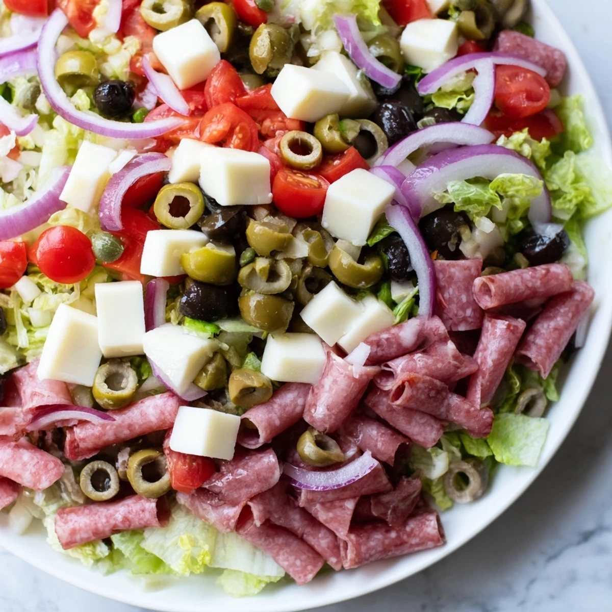 Chopped New Orleans Muffuletta Salad with olives, cured meats, cheeses, and tomatoes on a plate.