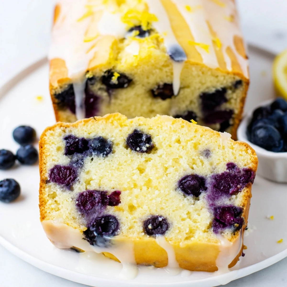 Freshly baked Lemon Blueberry Yogurt Loaf Cake on a rustic cutting board, with a slice missing and a cup of coffee nearby.