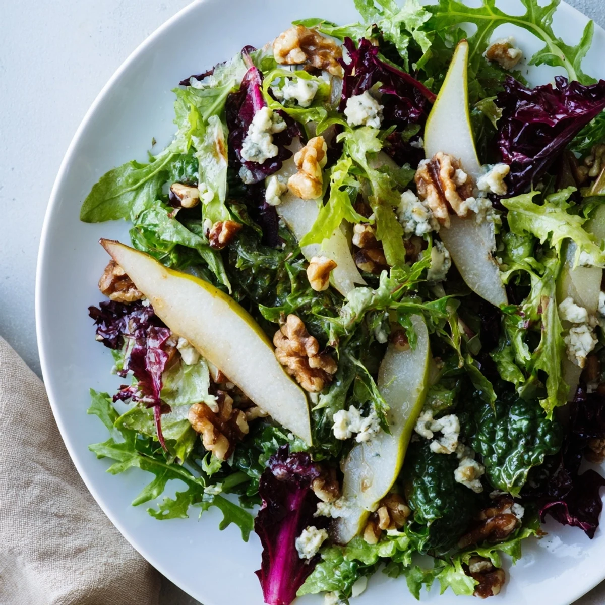 A vibrant Winter Green Salad with Pear and Walnuts showcases shiny walnuts, tender pear slices, and crumbled blue cheese, tossed in a bright apple cider vinaigrette for a refreshing bite.