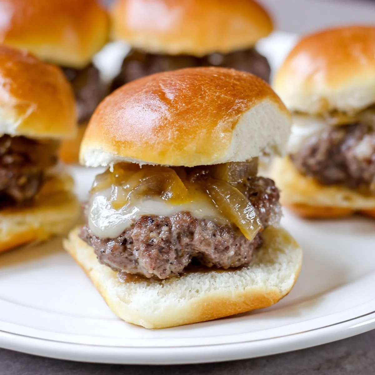 Tasty beef sliders topped with caramelized onions and cheese, paired with pickles and mustard on a plate.