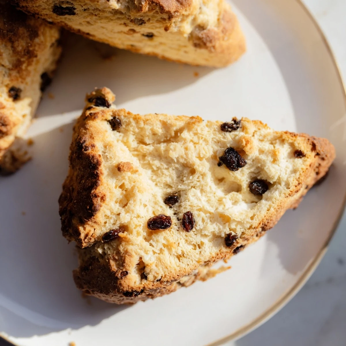 Eight wedges of Irish Soda Bread Scones with Currants arranged on a parchment-lined tray, brushed with buttermilk for a glossy finish.  