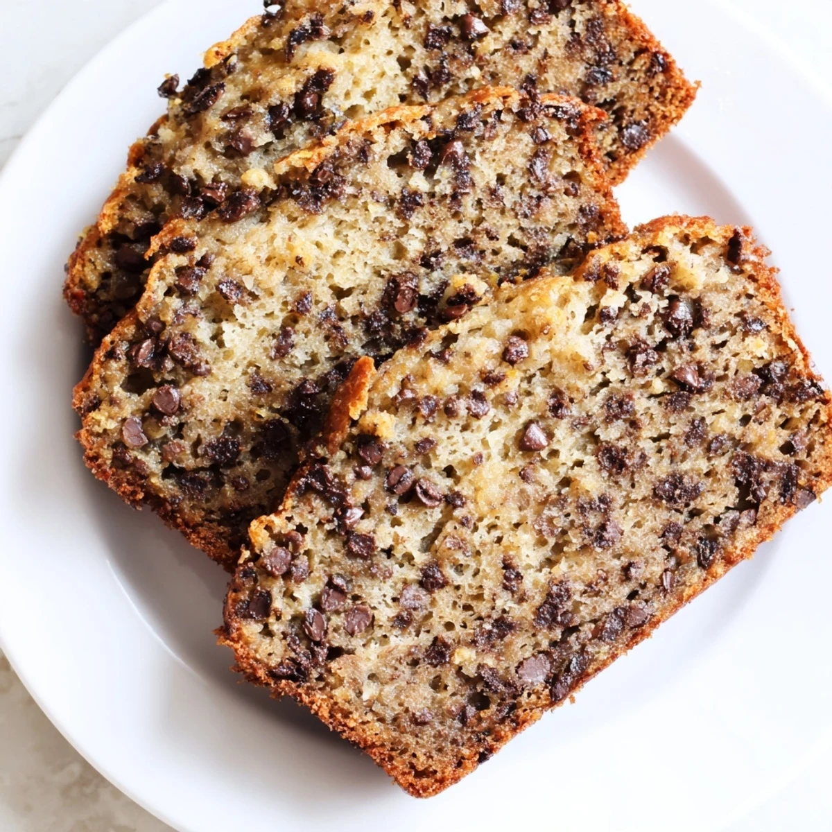 On a rustic kitchen counter, a loaf of Chocolate Chip Banana Bread cools on a wire rack, emitting sweet aromas of ripe bananas and cinnamon.