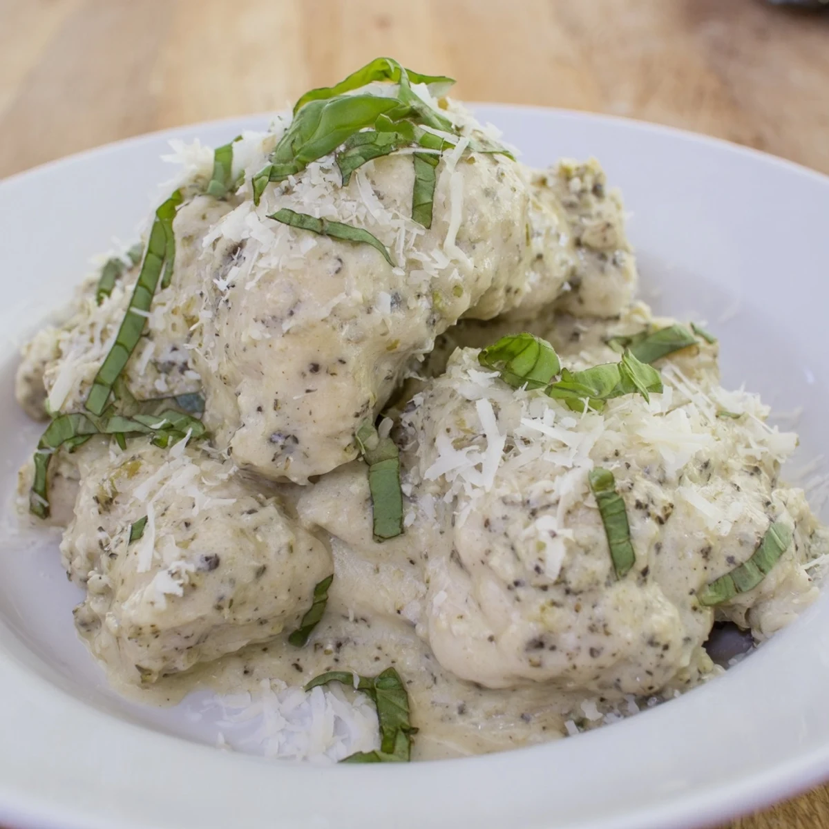 A close-up of Pesto Ranch Crock Pot Chicken Thighs on a plate with roasted vegetables and a rich sauce.