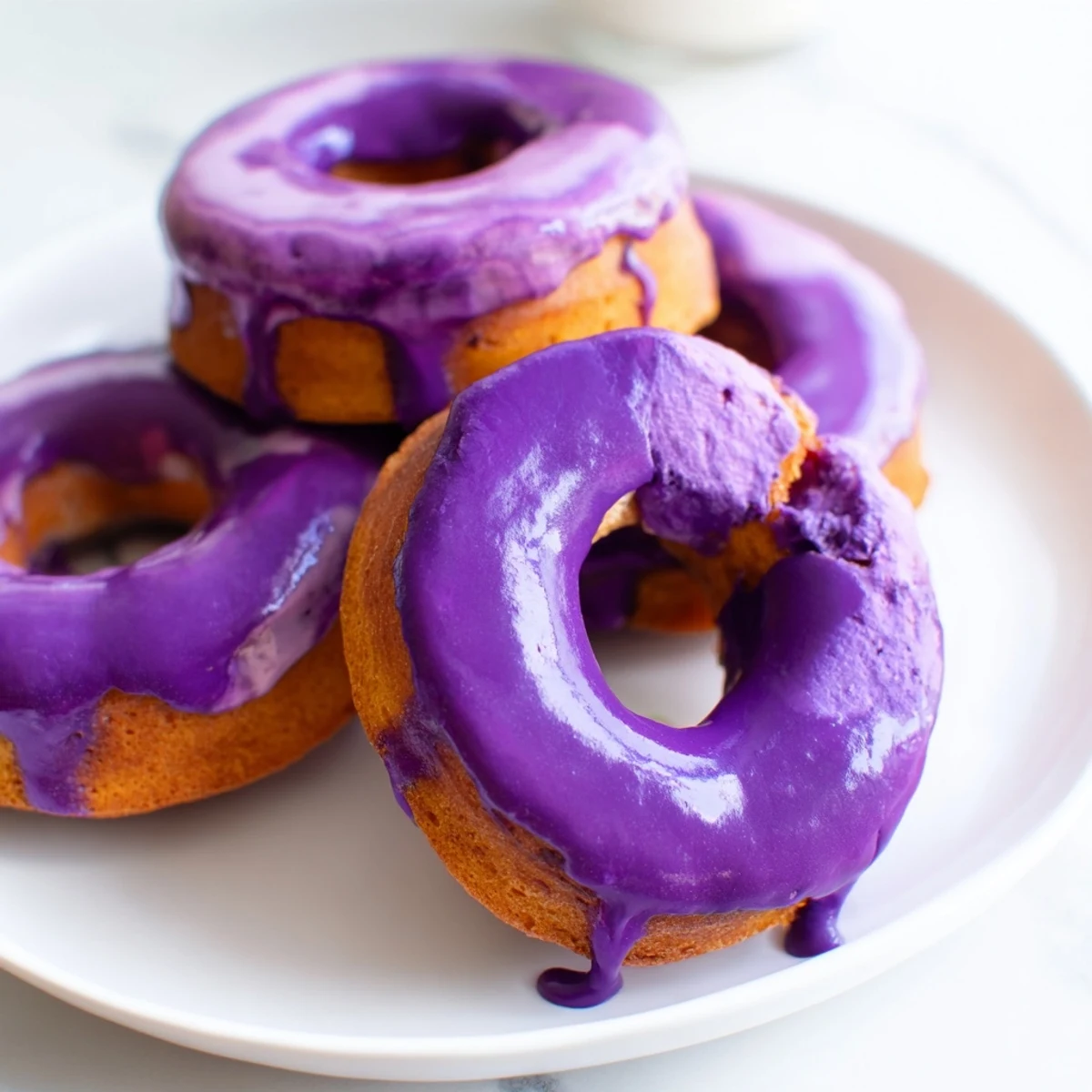 A close-up of Ube Mochi Donuts drizzled with sweet glaze, served on a plate alongside a steaming cup of coffee.
