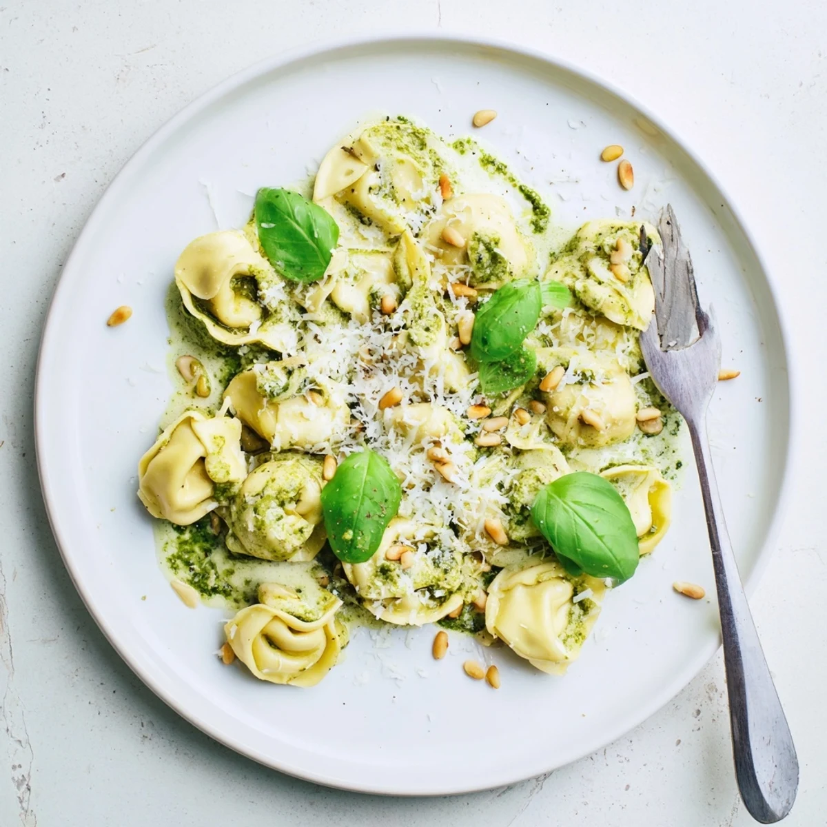 Steaming Pesto Alfredo Tortellini tossed in a rich green sauce, ready to be served for a cozy dinner.