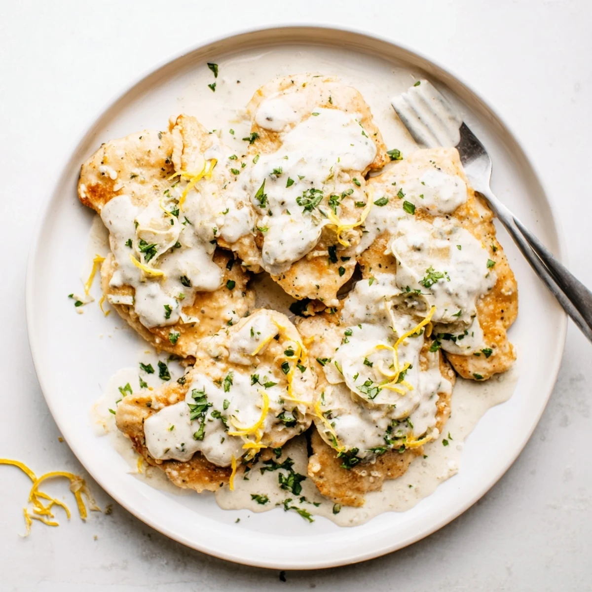 Close up of Creamy Parmesan Lemon Chicken with a spoonful of sauce drizzled over the chicken, showing rich texture.