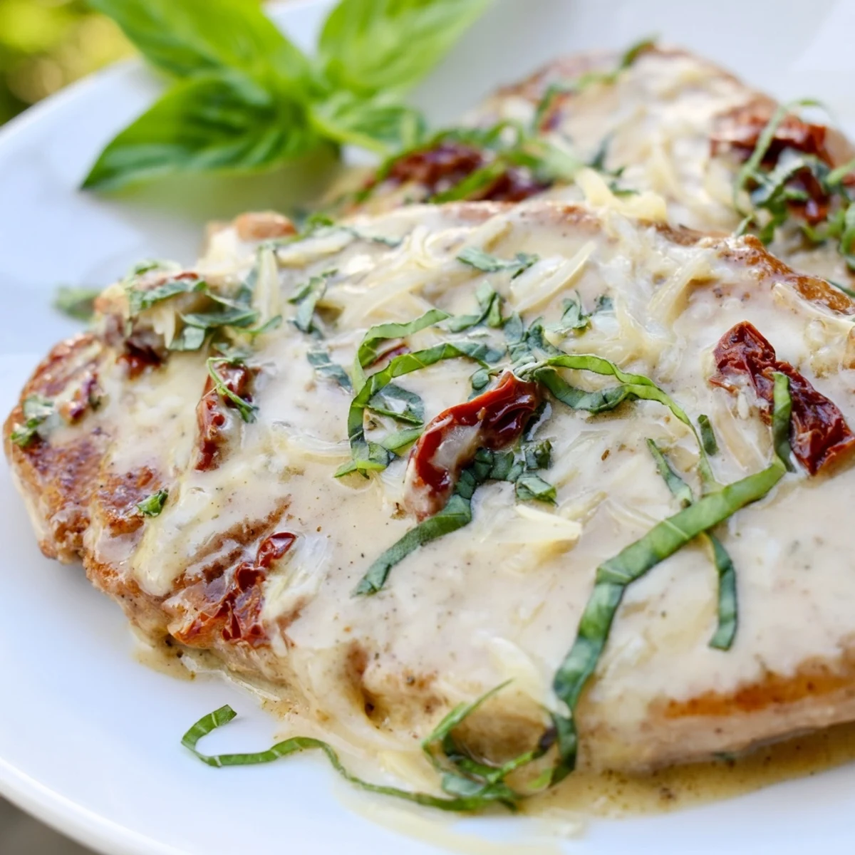 Golden brown Marry Me pork chops resting in creamy sun-dried tomato parmesan sauce garnished with fresh basil