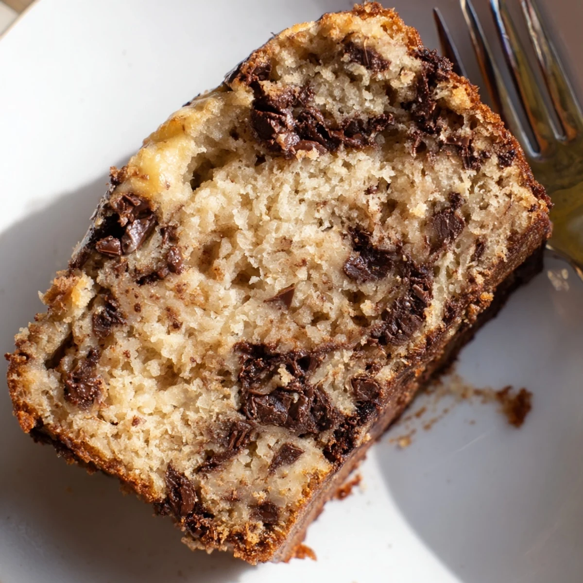 Golden chocolate chip banana bread loaf with melted chocolate speckles on a rustic wooden board