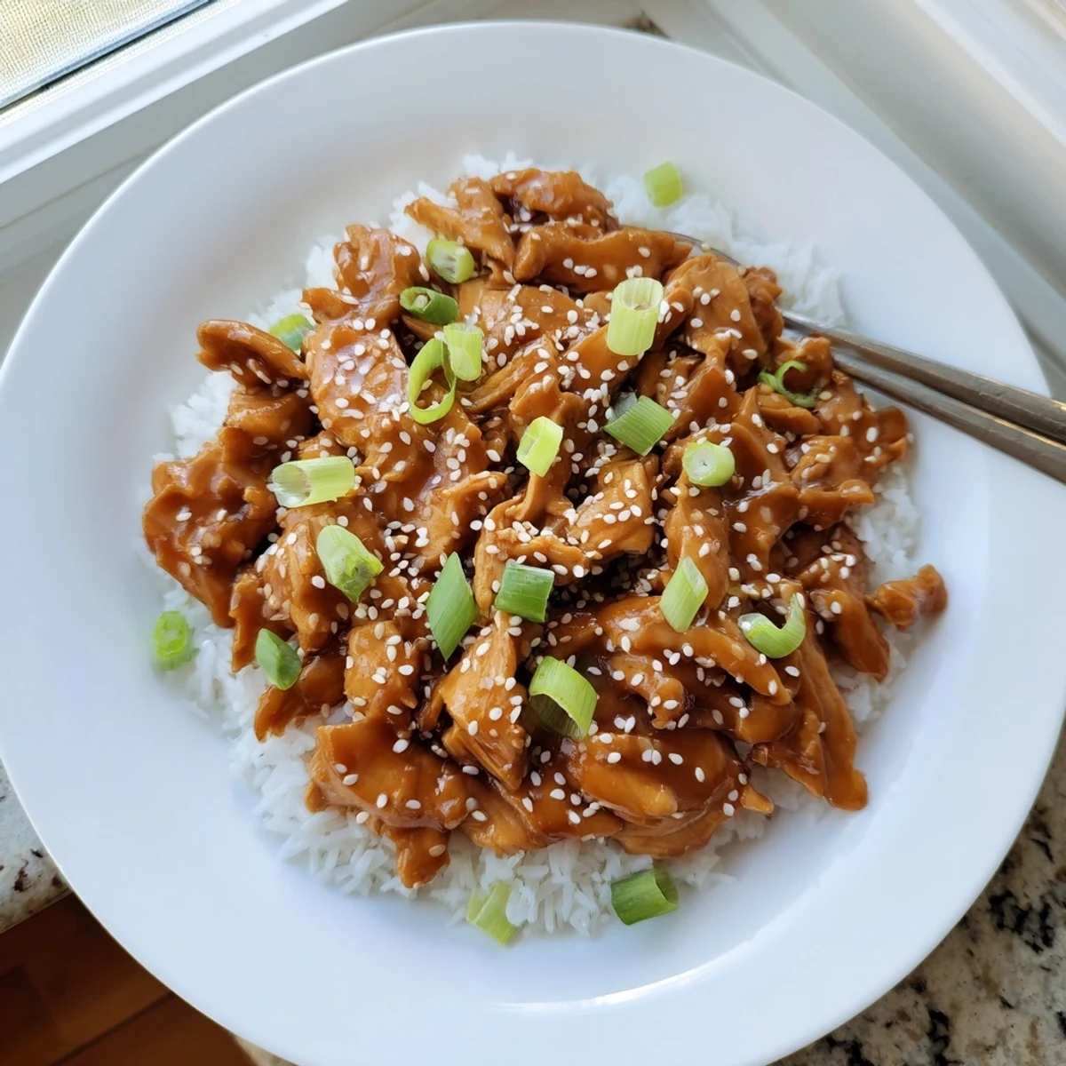 Slow cooker sesame chicken pieces coated in glossy brown sauce and sprinkled with white sesame seeds