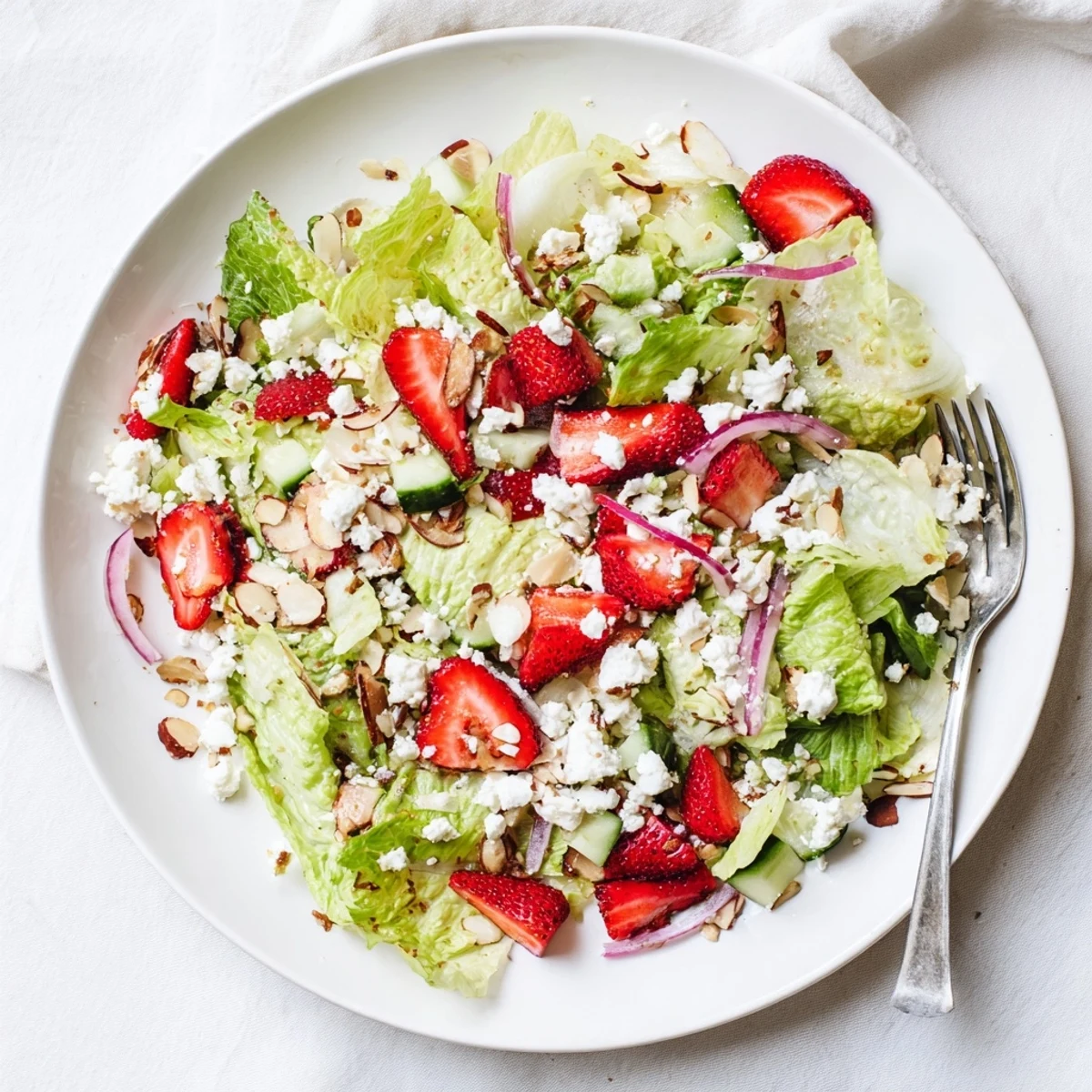 Vibrant layered salad bowl featuring crisp romaine, juicy strawberries, crumbled feta, and sliced almonds