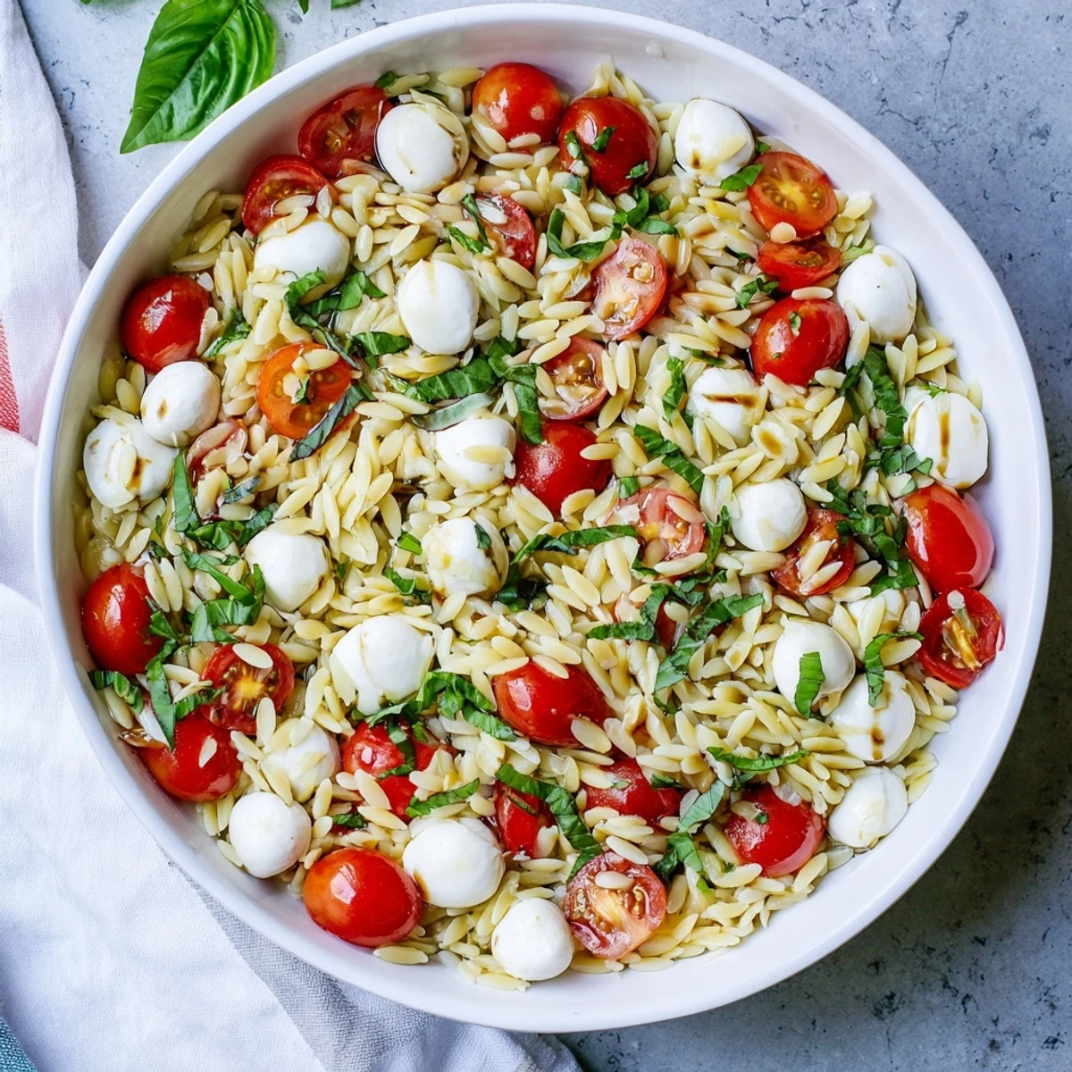 Colorful bowl of Caprese orzo pasta salad drizzled with tangy balsamic vinaigrette and torn basil