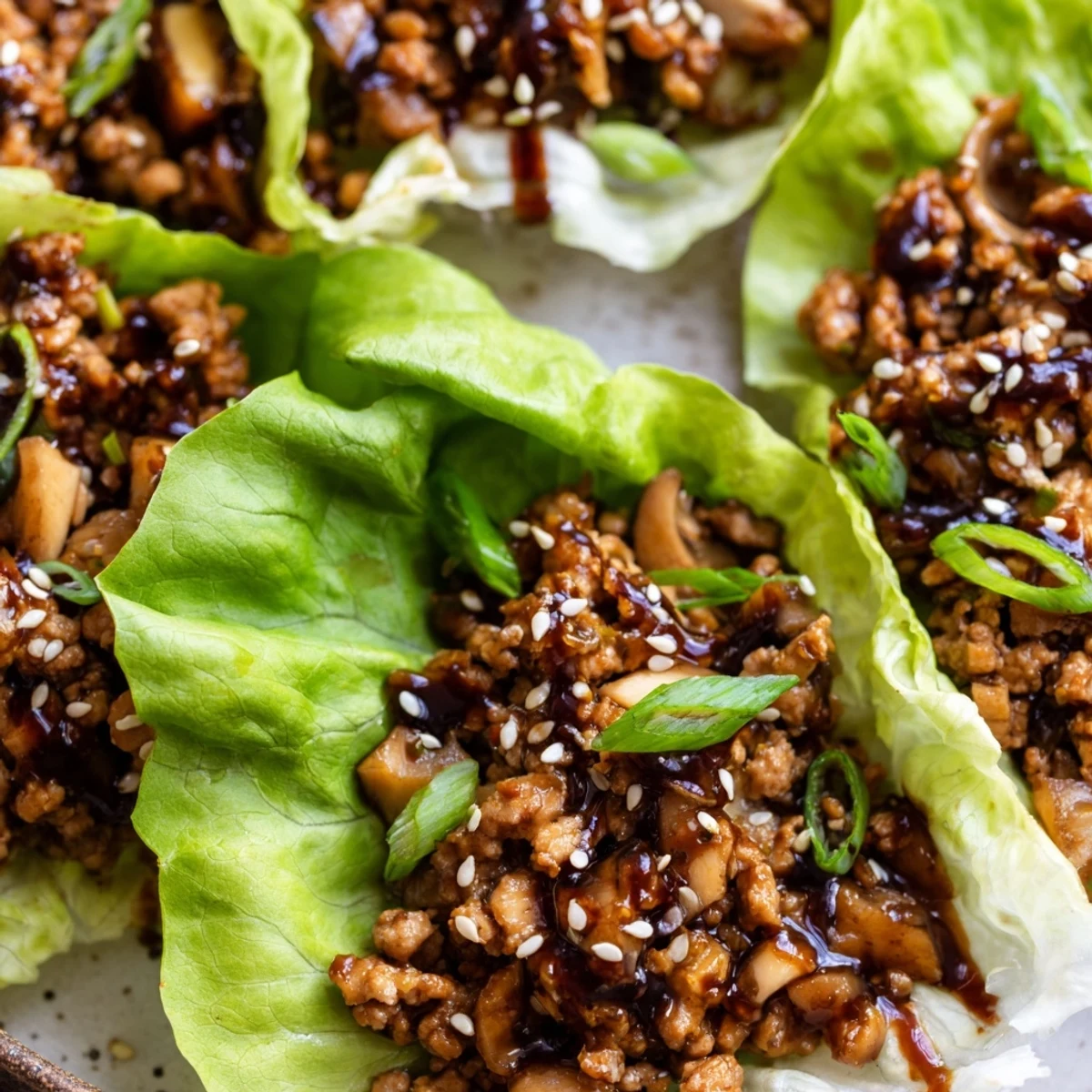 Easy chicken lettuce wraps garnished with sesame seeds and sliced scallions on a white plate