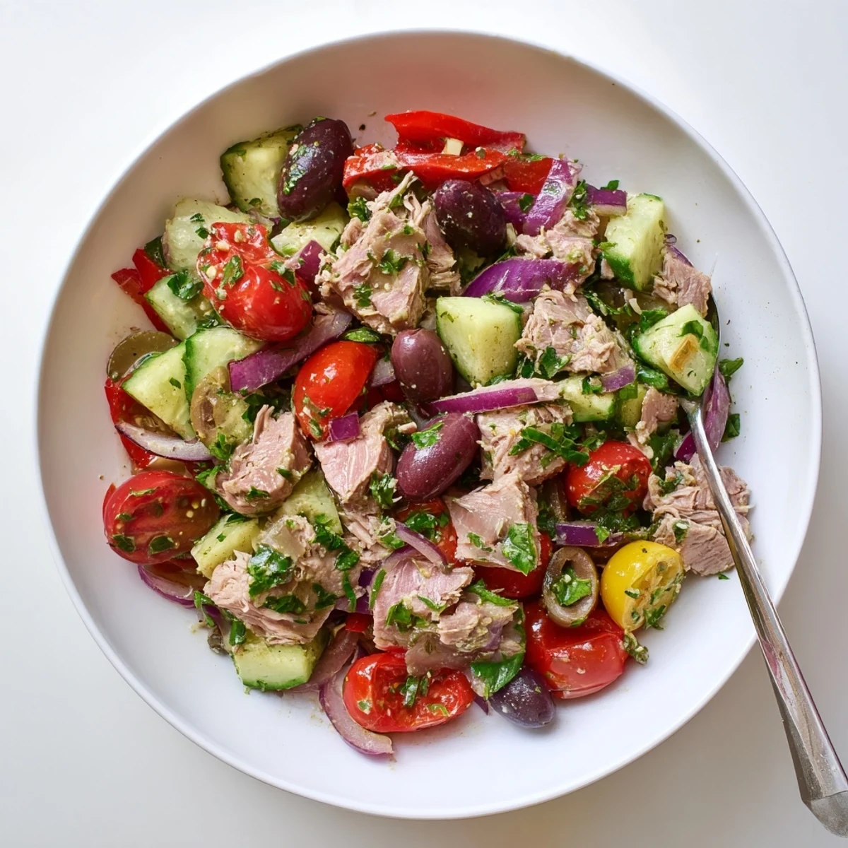 Colorful Mediterranean tuna salad mounded in a white bowl with fresh herbs, tomatoes, and olives glistening under lemon dressing