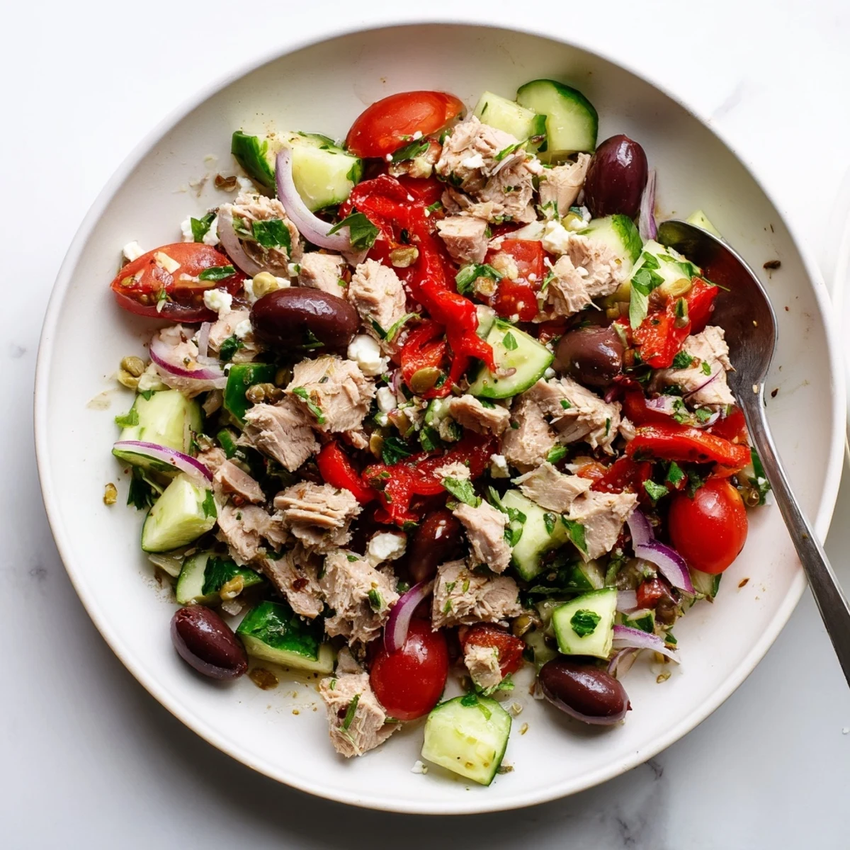 Vibrant Mediterranean tuna salad bowl topped with crumbled feta, fresh parsley, and basil beside a slice of crusty whole grain bread