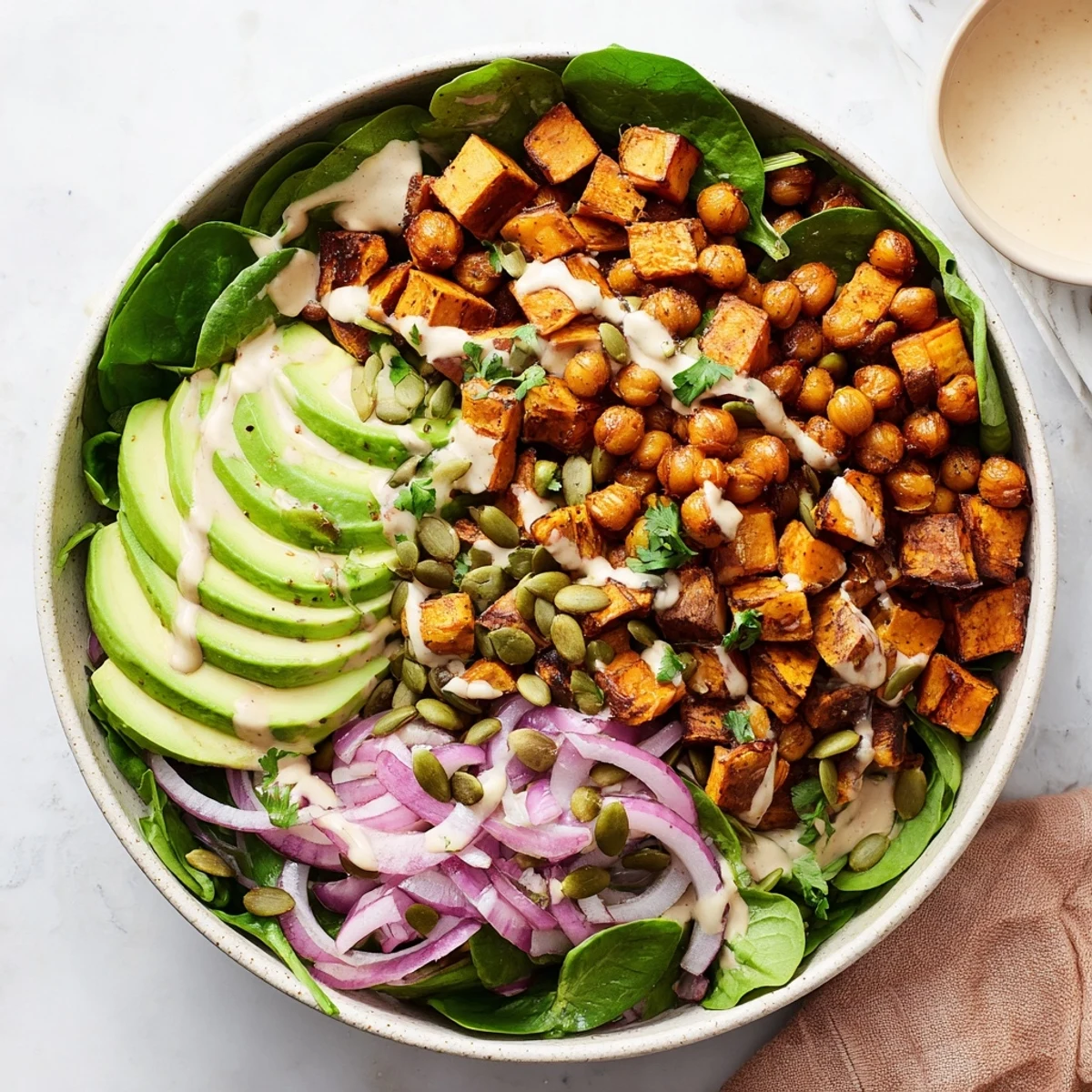 Golden roasted sweet potato and chickpea bowls drizzled with creamy tahini dressing over fresh baby spinach