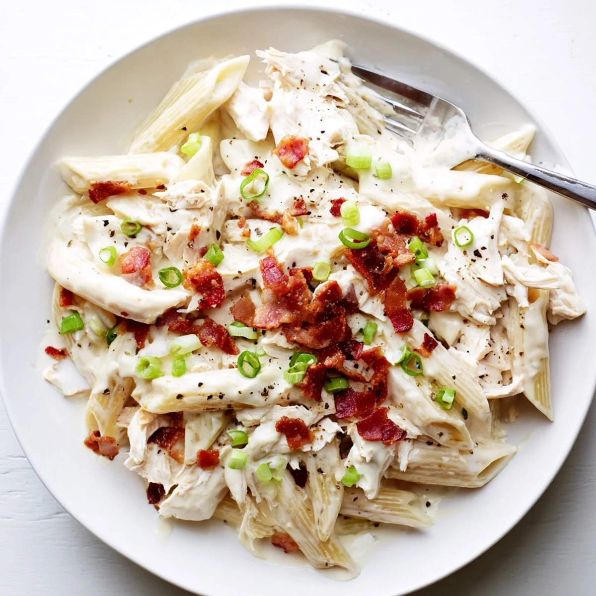 Comforting crack chicken pasta bowl topped with green onions, parmesan, and savory bacon bits over penne noodles.