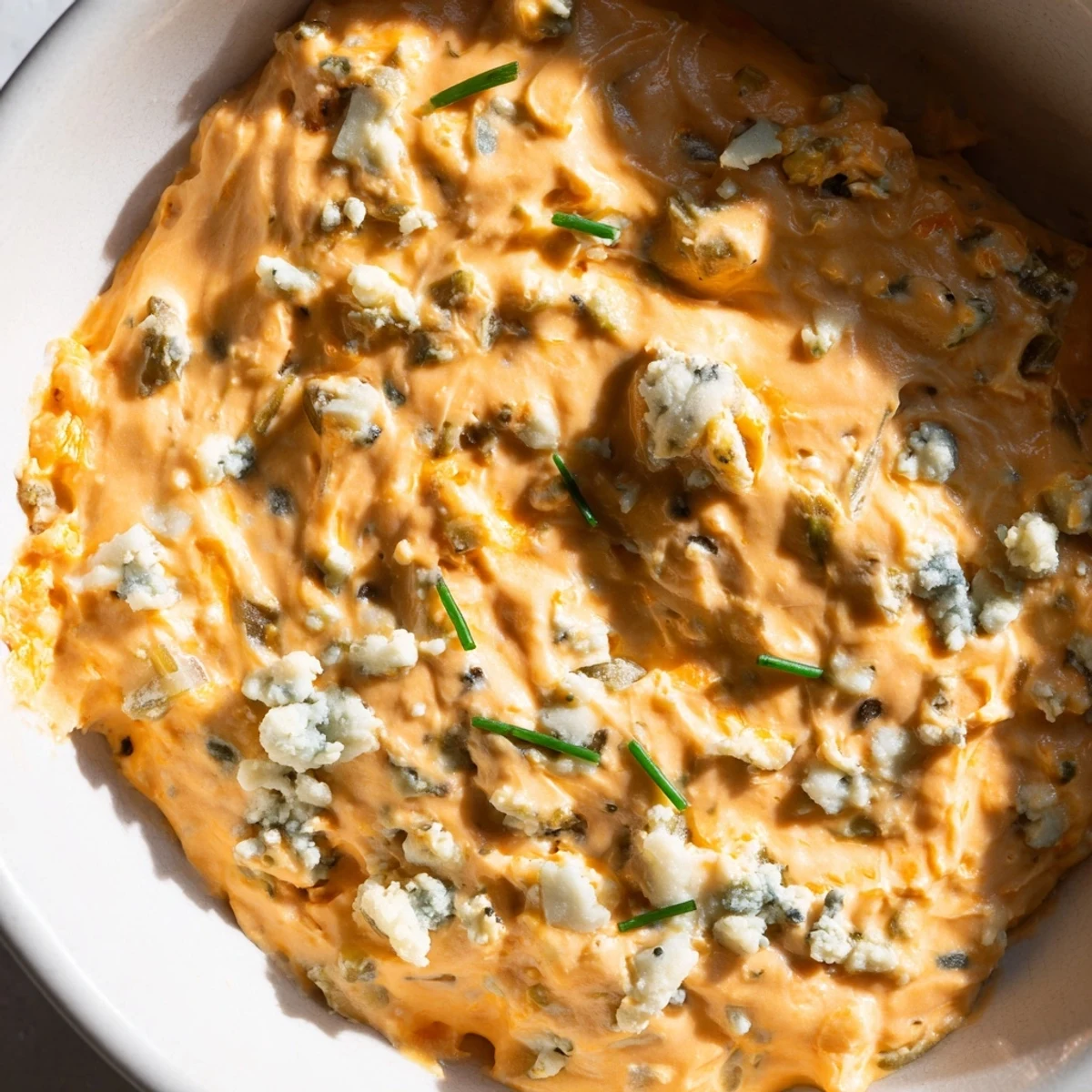 Creamy Buffalo Pickle Dip in a bowl garnished with fresh chives and pickle slices