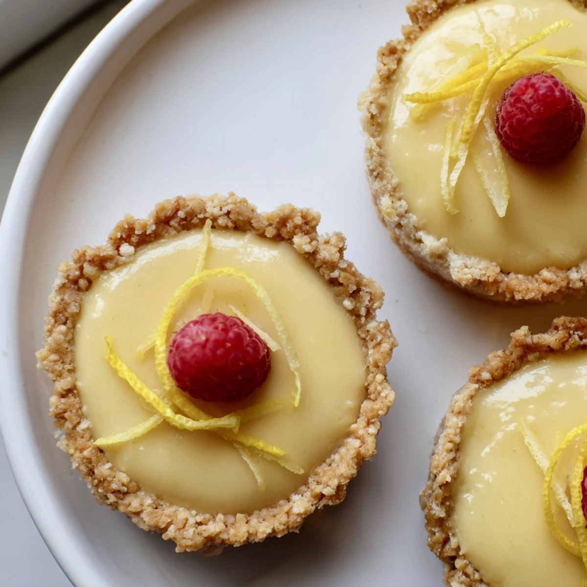 Golden mini vegan lemon tarts topped with fresh berries on a rustic baking sheet