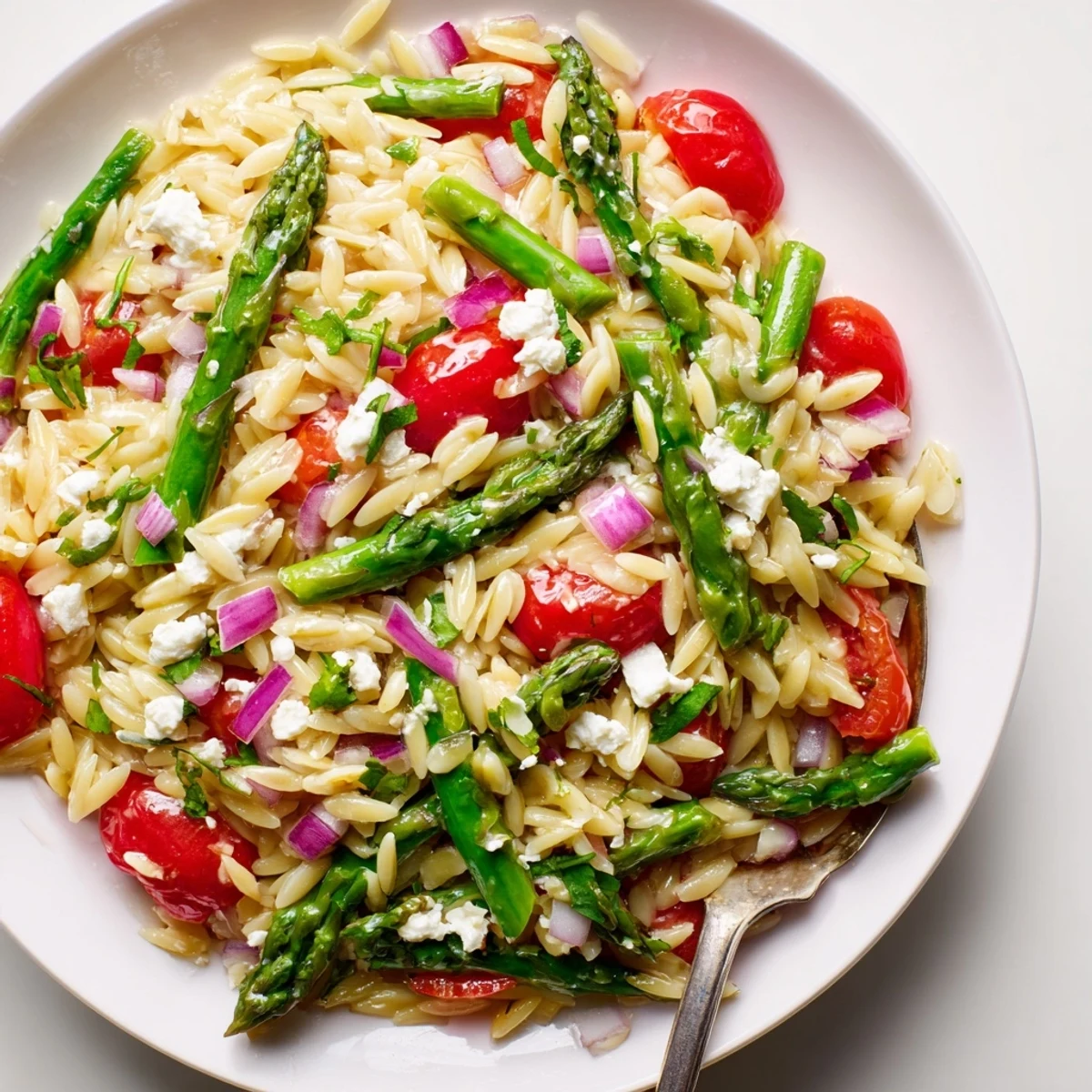 Asparagus Orzo Salad With Lemon Vinaigrette chilled on table, feta and parsley garnish.