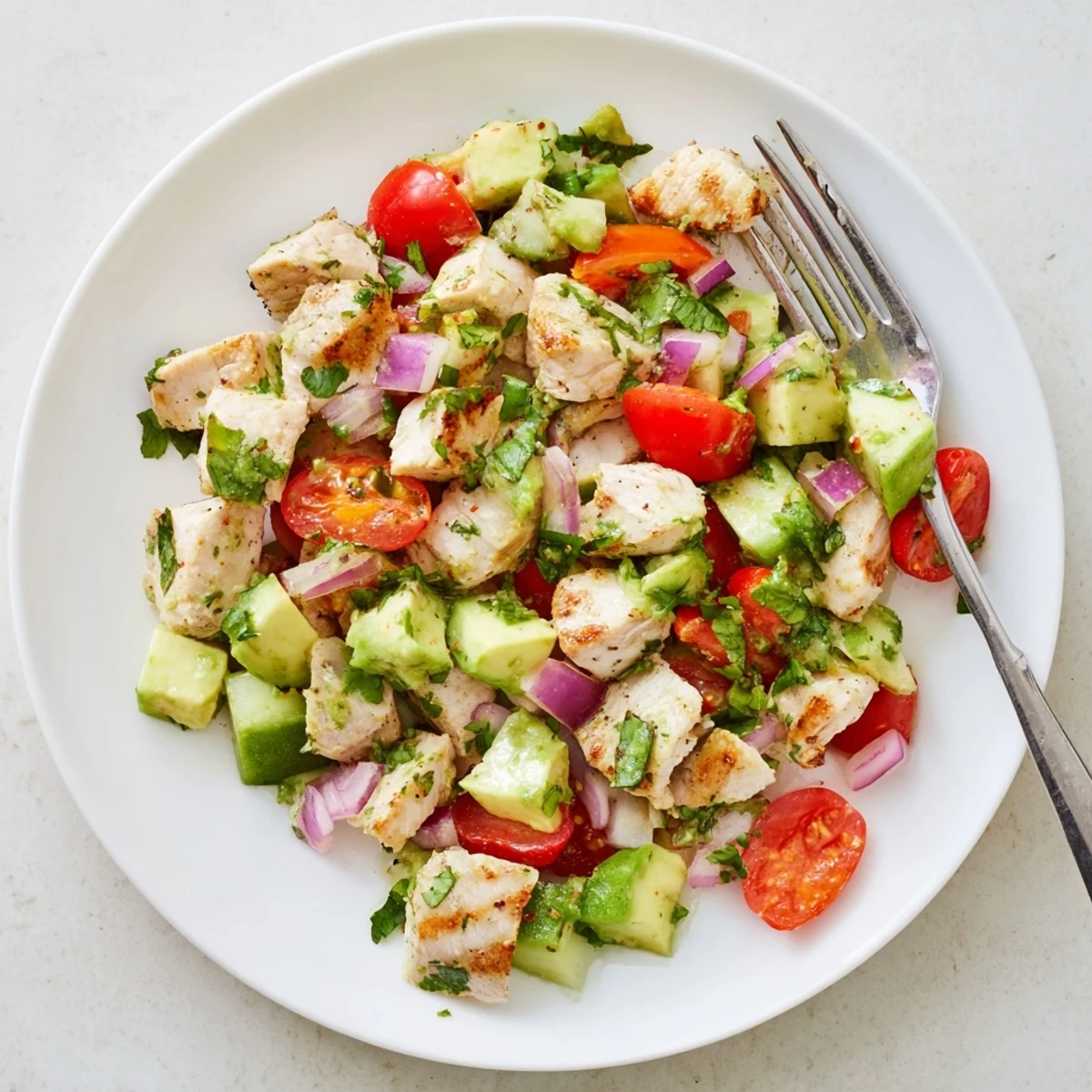 Glowing bowl of healthy avocado chicken salad topped with diced avocado, tomatoes, cucumber, and zesty lime dressing