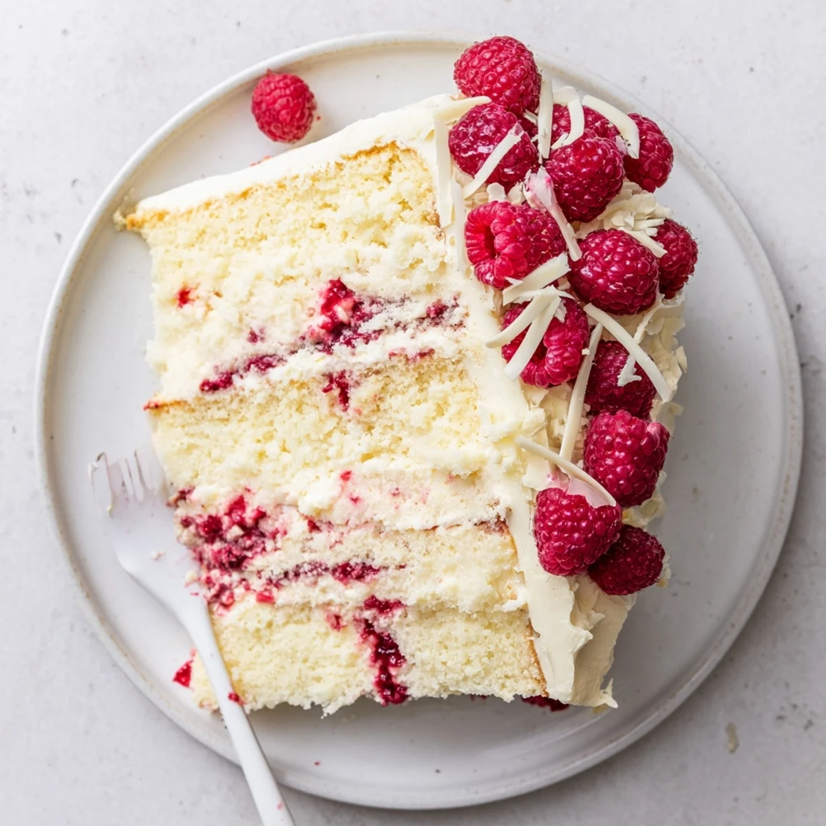 Slice of white chocolate raspberry dream cake showing white chocolate curls and vibrant red raspberry layers