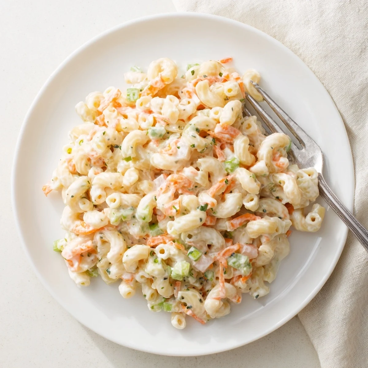 Creamy Hawaiian macaroni salad piled high with grated carrots and celery in a white serving bowl