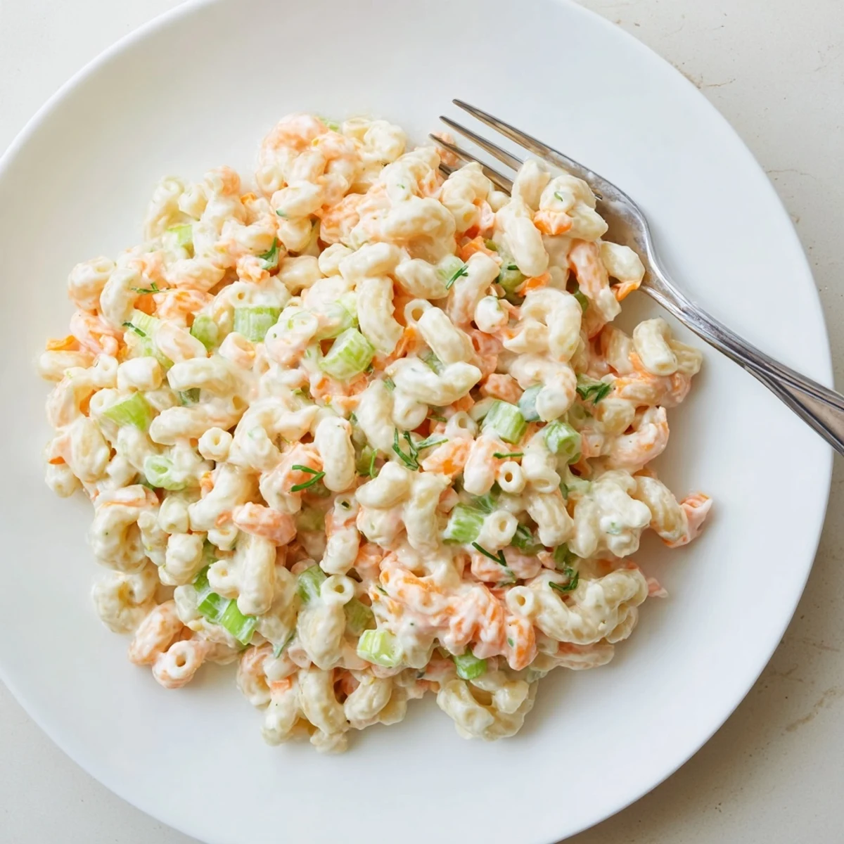 Golden elbow macaroni coated in tangy mayonnaise dressing with colorful chopped vegetables throughout