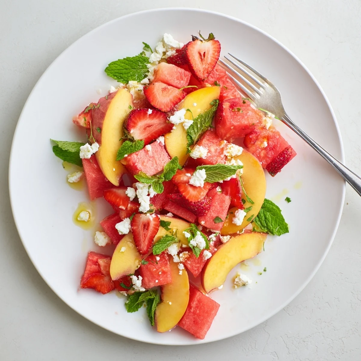 Juicy summer peach watermelon salad with ripe strawberries and torn mint leaves garnish