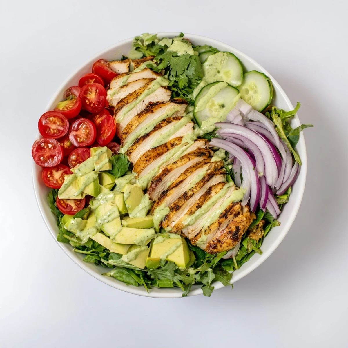 Colorful layered salad bowl featuring juicy spiced chicken and creamy avocado yogurt dressing