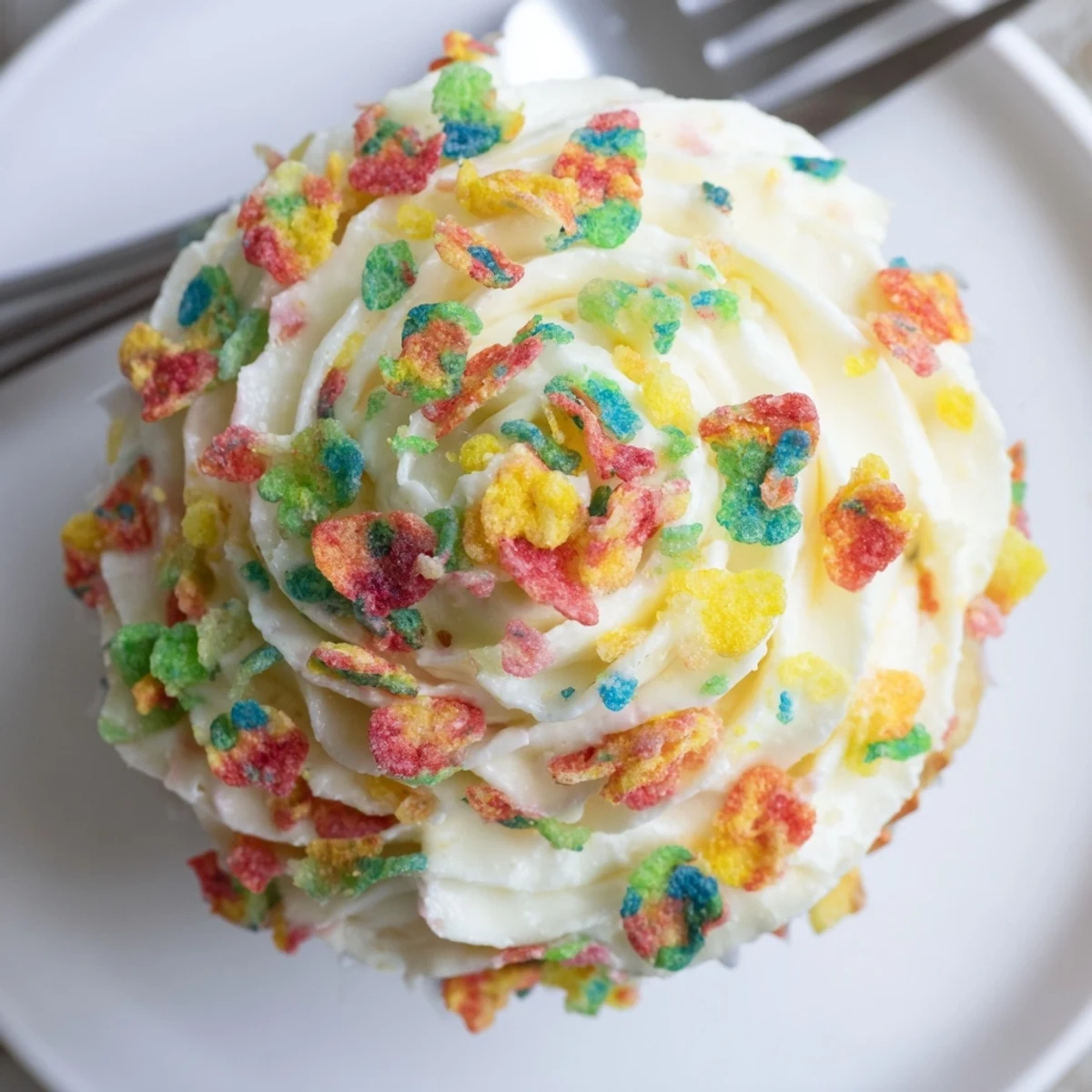 Close-up of a cupcake topped with Fruity Pebbles Cereal Frosting, creamy rainbow crunch