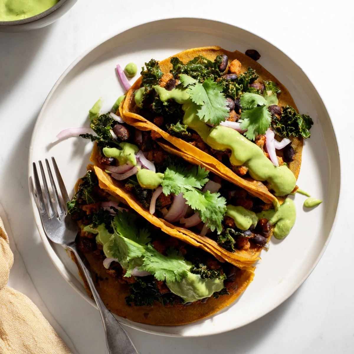 Smoky black bean kale tacos drizzled with vibrant creamy green sauce on warm tortillas