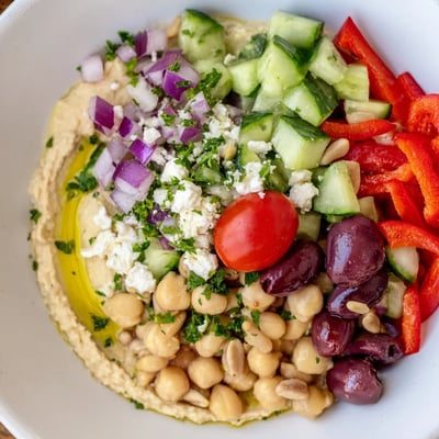 Fresh Mediterranean Salad with Hummus showcases diced bell peppers, Kalamata olives, and a creamy hummus base, perfect for a light lunch.