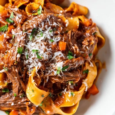A bowl of tender shredded Slow Cooker Beef Ragu, garnished with fresh parsley and served with al dente pasta.