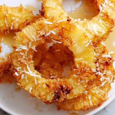 A close-up of a crispy fried pineapple ring topped with a scoop of vanilla ice cream melting beside it.