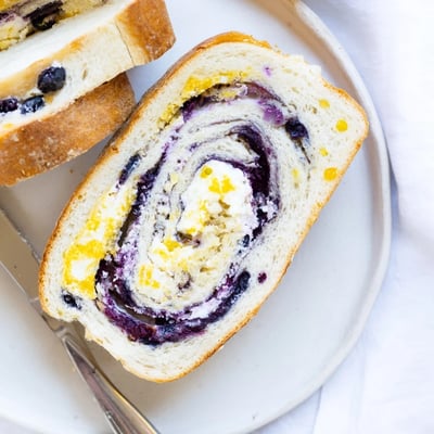 A moist slice of Blueberry Lemon Cream Cheese Sourdough with creamy cheese swirls on a plate.