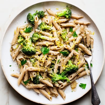 A close-up view of a warm serving of Easy Healthy Broccoli Pasta featuring tender green vegetables and al dente noodles on a rustic wooden table.