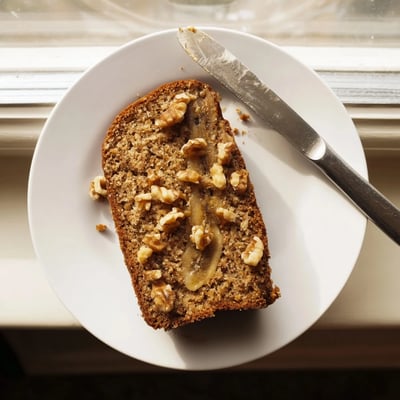Moist banana nut bread sliced on a rustic board with scattered walnut pieces